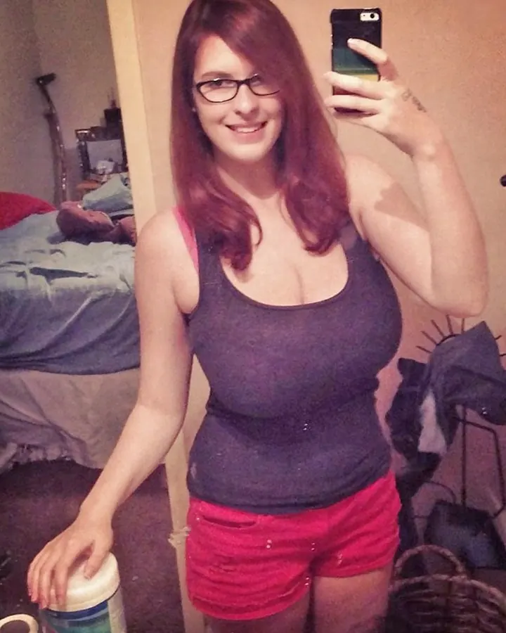 Femme en t-shirt noir et shorts blancs, prenant un selfie, regardant l'appareil.