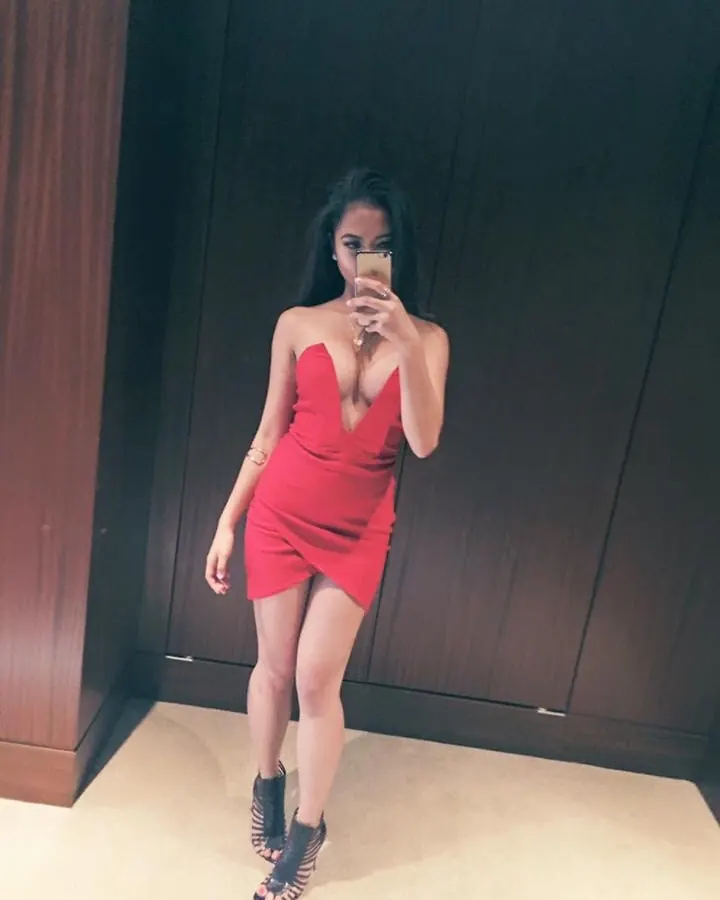 Femme arabe aux cheveux bruns, en sous-vêtements roses, prenant un selfie devant un miroir dans une salle de bain.