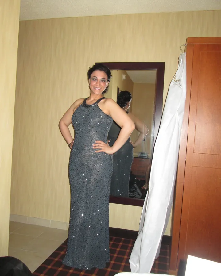 Femme arabe de 35 à 45 ans en tenue de Noël rouge, posant de dos devant une grande fenêtre avec vue sur une ville.
