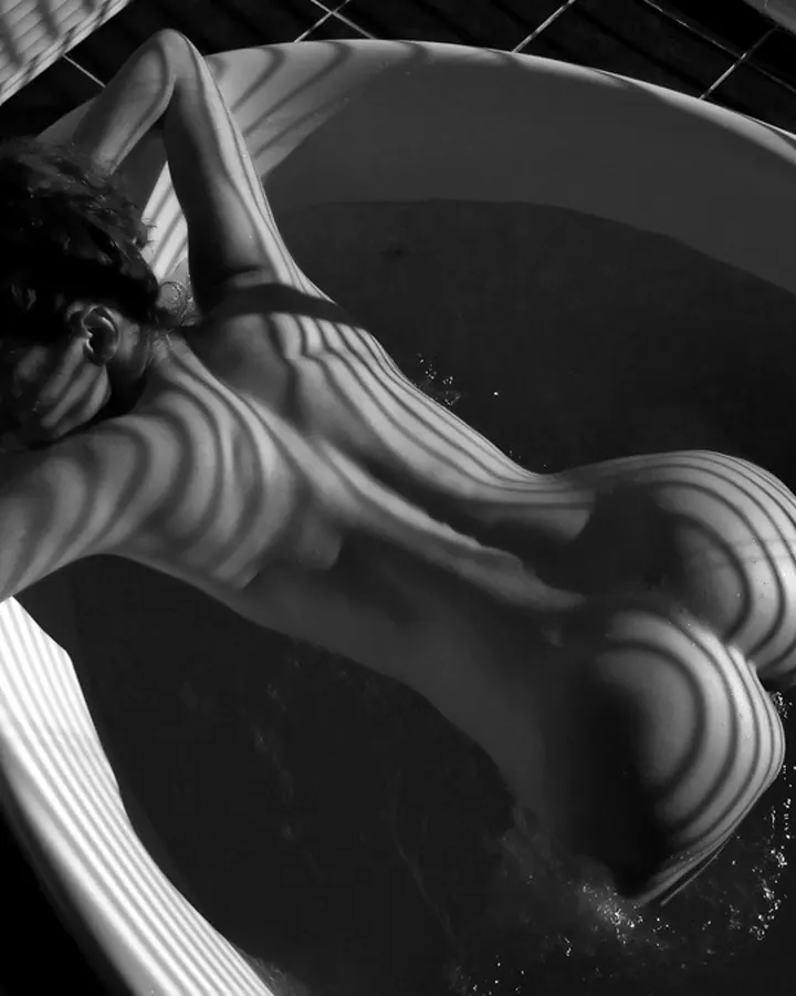 Femme arabe entre 25 et 35 ans, en haut noir, se tenant près d'un canapé blanc dans un salon lumineux.
